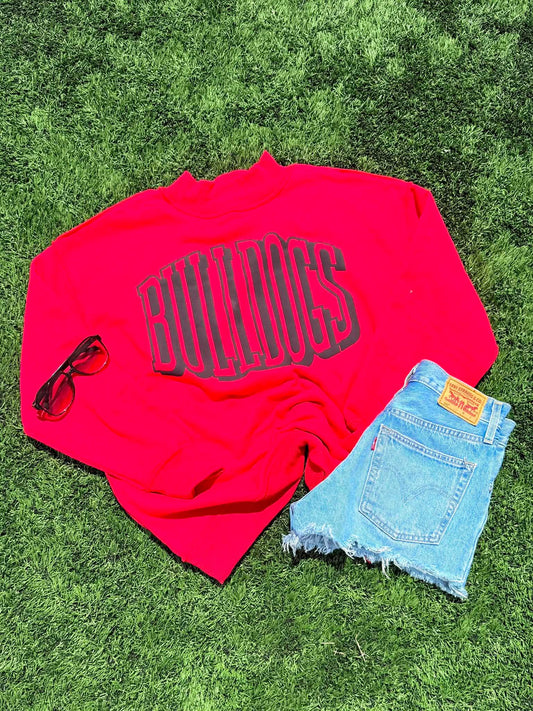 Red shirt with 'Bulldogs' text, sunglasses, and denim shorts on grass