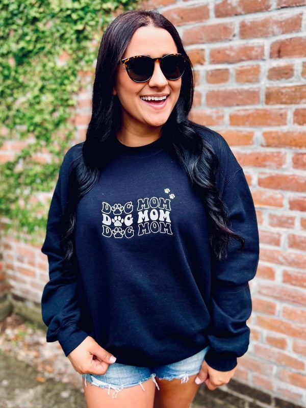 A woman smiling and wearing a black sweatshirt with the text 'Dog Mom' and a small wave symbol embroidered on it.
