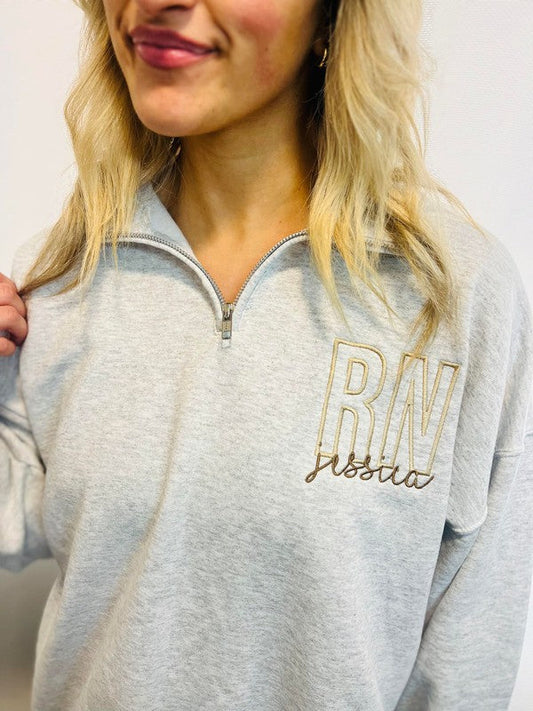 A woman wearing a gray sweatshirt with 'RN' embroidered on the front.