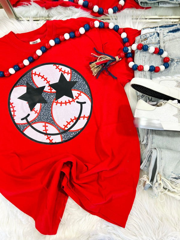 A red graphic tee with a baseball and stars design, accompanied by blue and white beaded necklaces and a black hair tie.