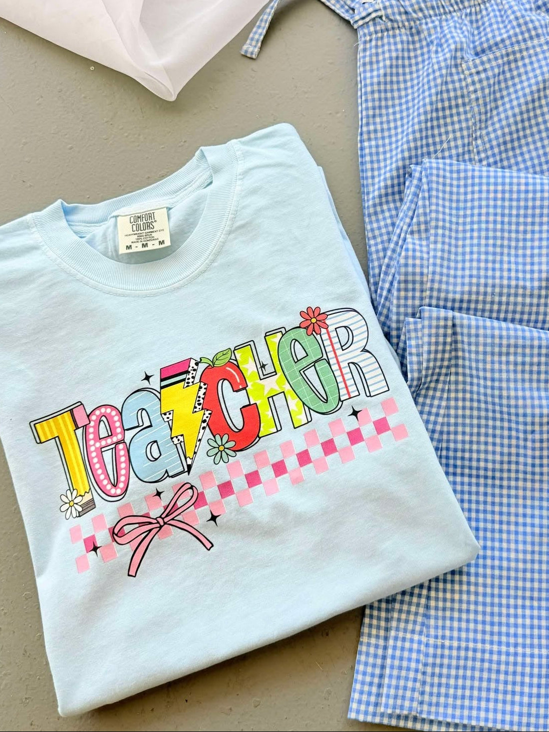 Folded t-shirt with 'TEACHER' text on a checkered fabric background