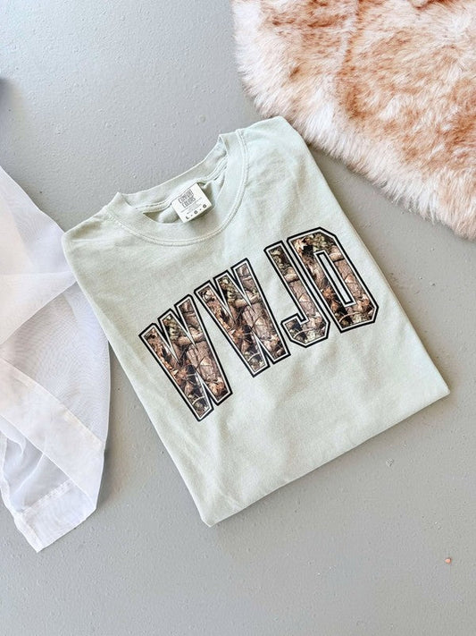A white t-shirt with 'WWJD' camouflage pattern printed on it, displayed flat with a tag and a furry item in the background.