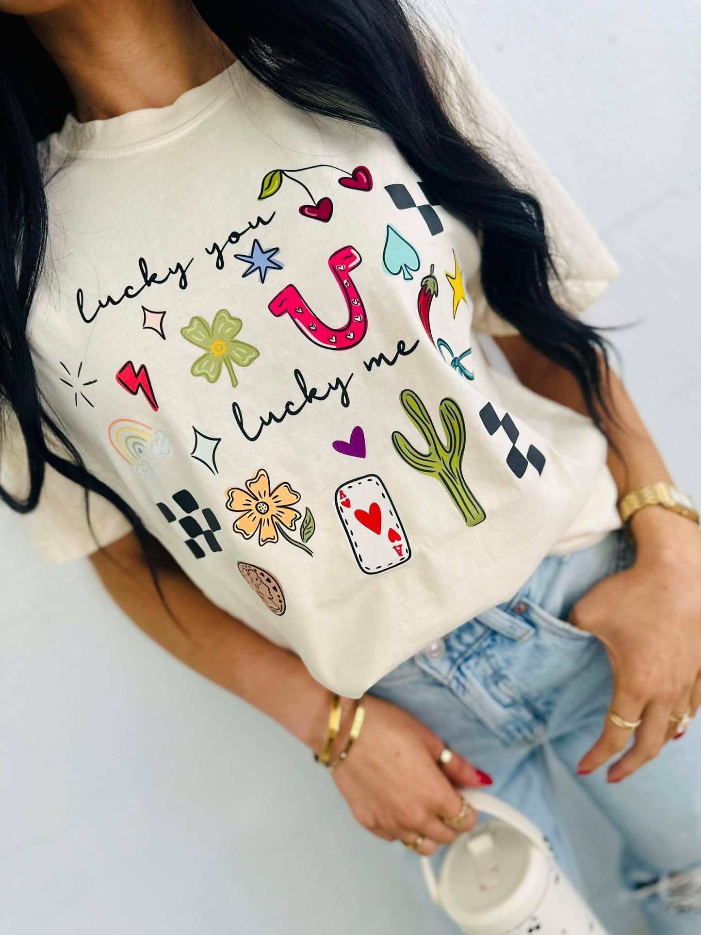 Person wearing a white t-shirt with colorful lucky you lucky me western cowboy graphics and text.