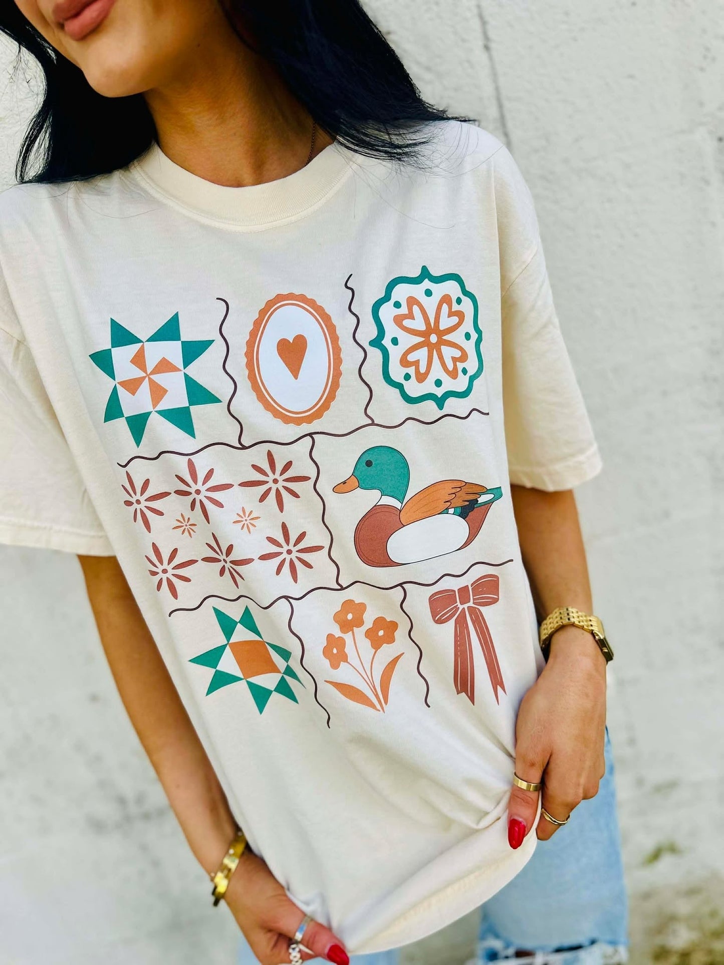Person wearing a white t-shirt with colorful Antique Designs patterns and a mallard duck illustration.