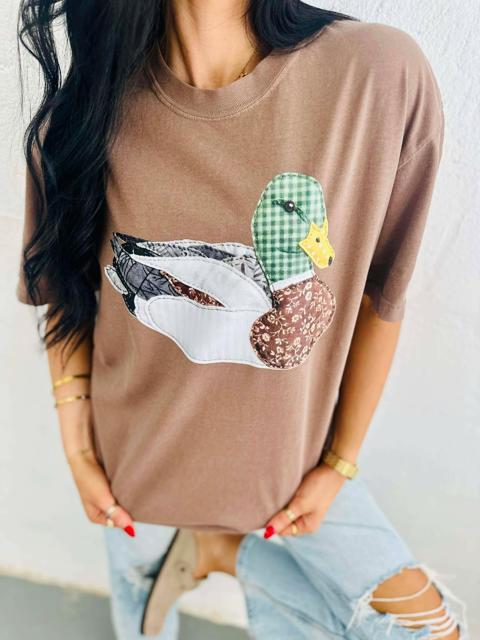 Person wearing a brown t-shirt with a viral patchwork mallard duck graphic design.