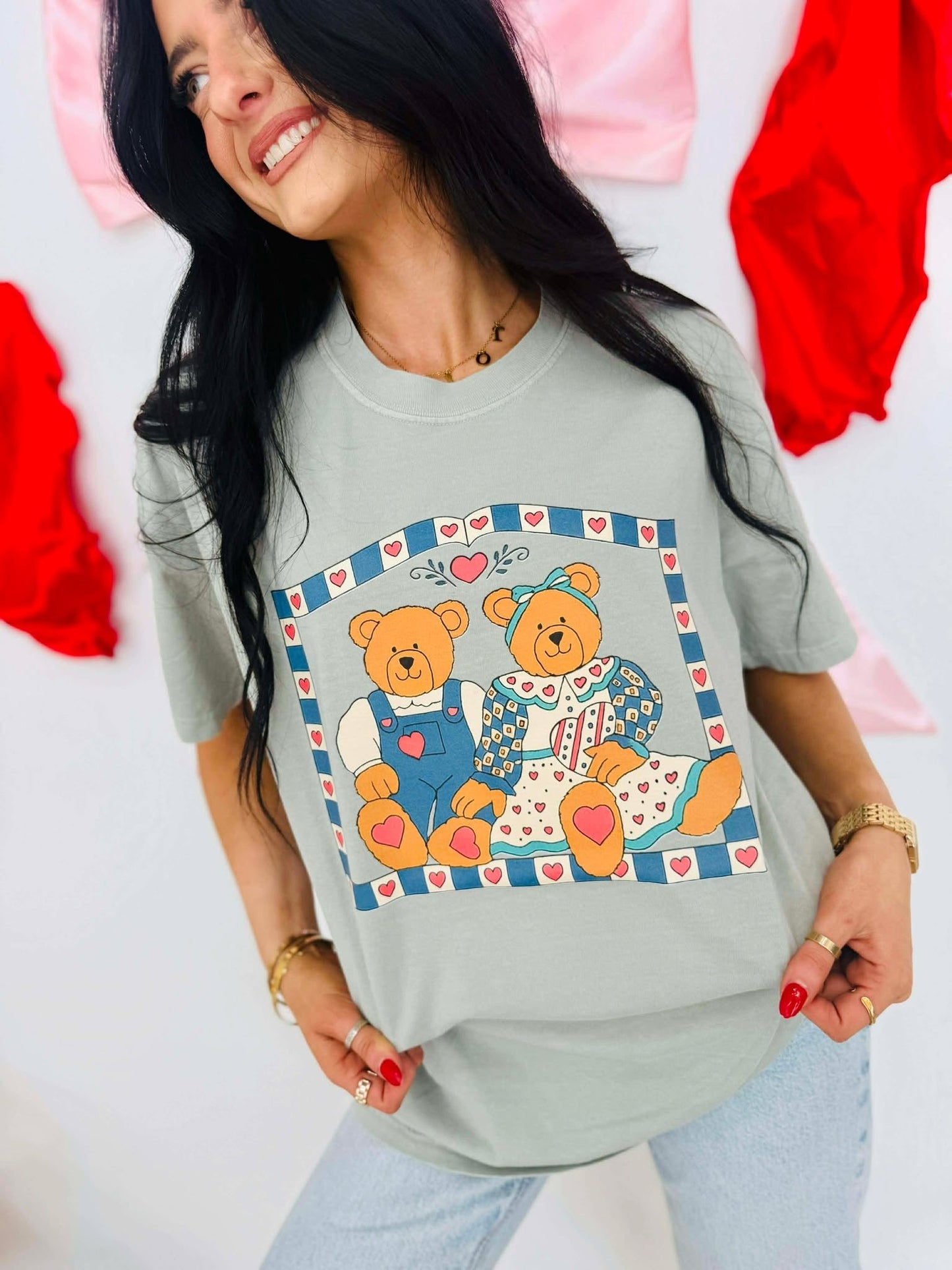 Woman wearing a light gray t-shirt with teddy bear design, standing against a colorful background.