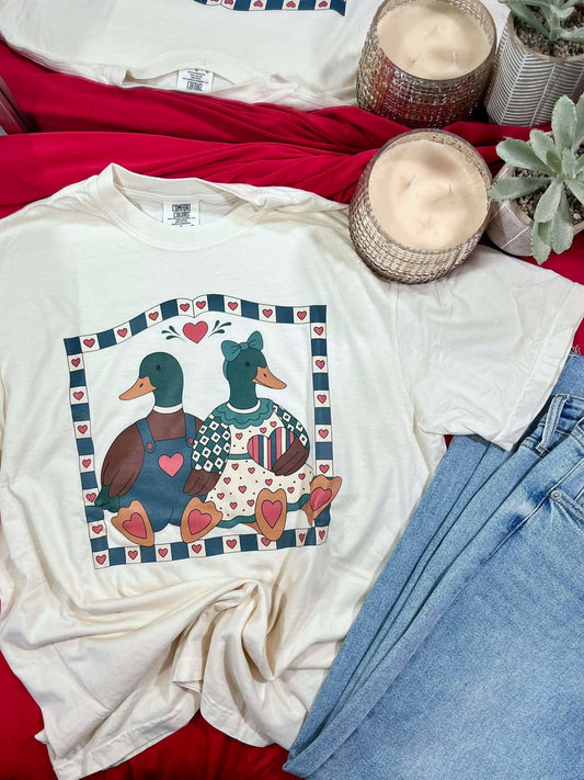 White t-shirt with duck design on a red surface with jeans and candles.