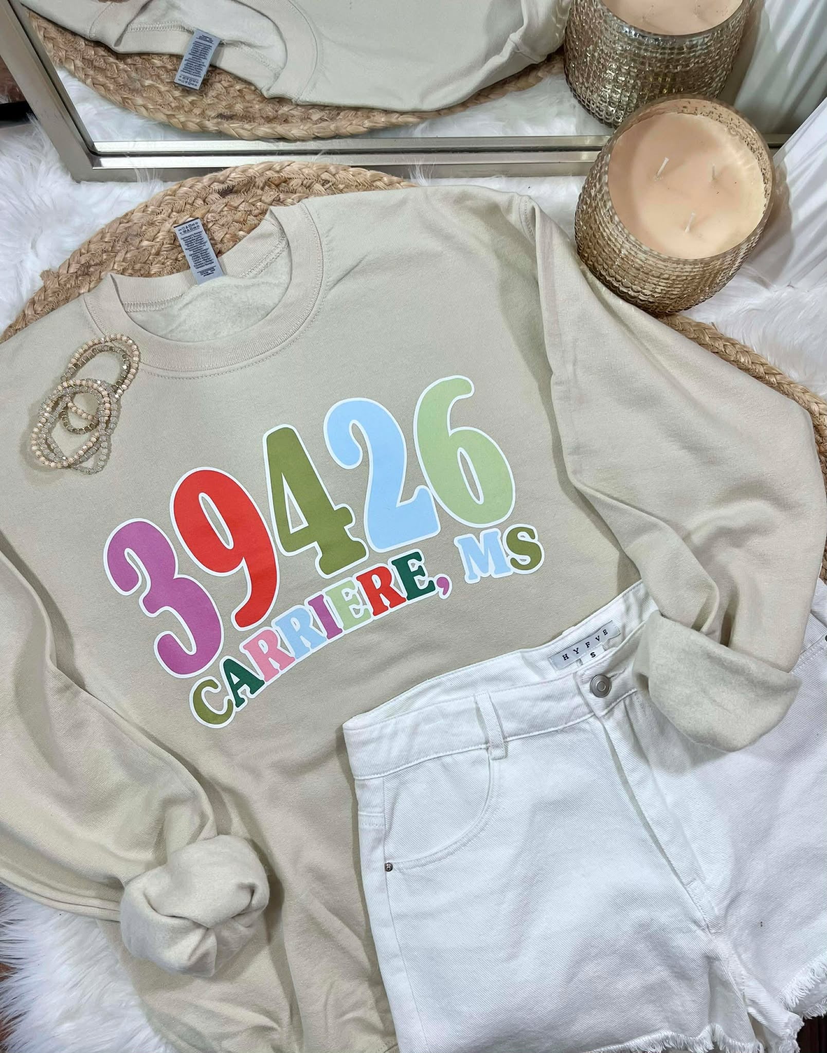 Beige sweatshirt with colorful zipcode  text on a bed