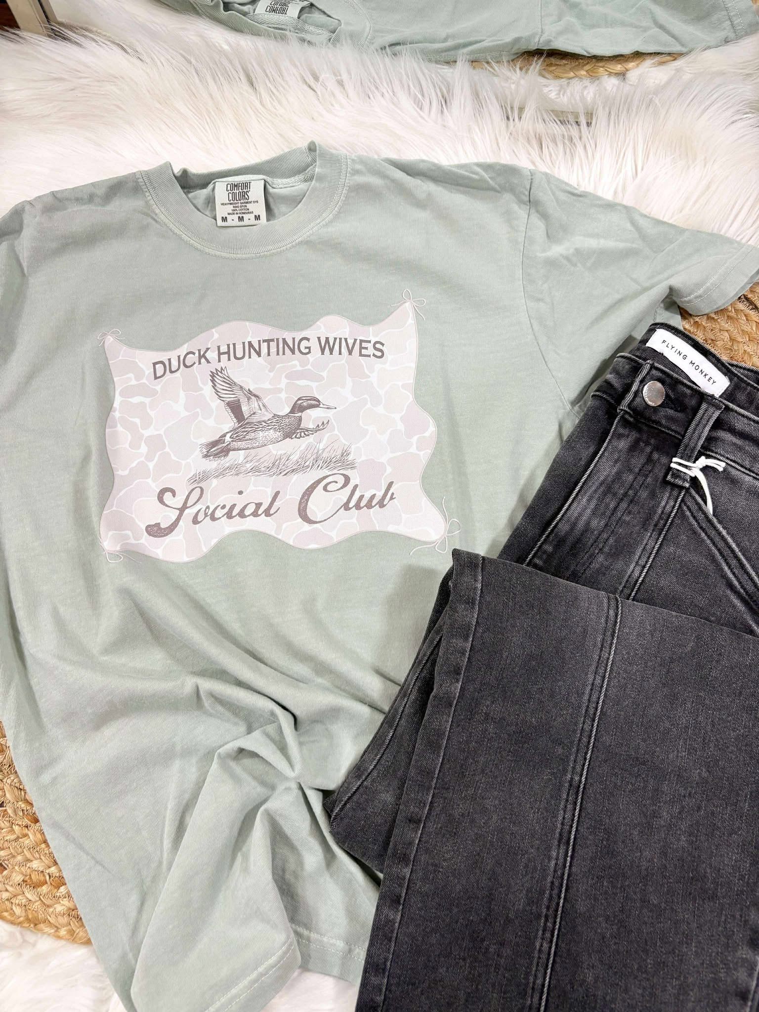 Light green t-shirt with Duck Hunting Wives Social Club graphic design on a textured surface