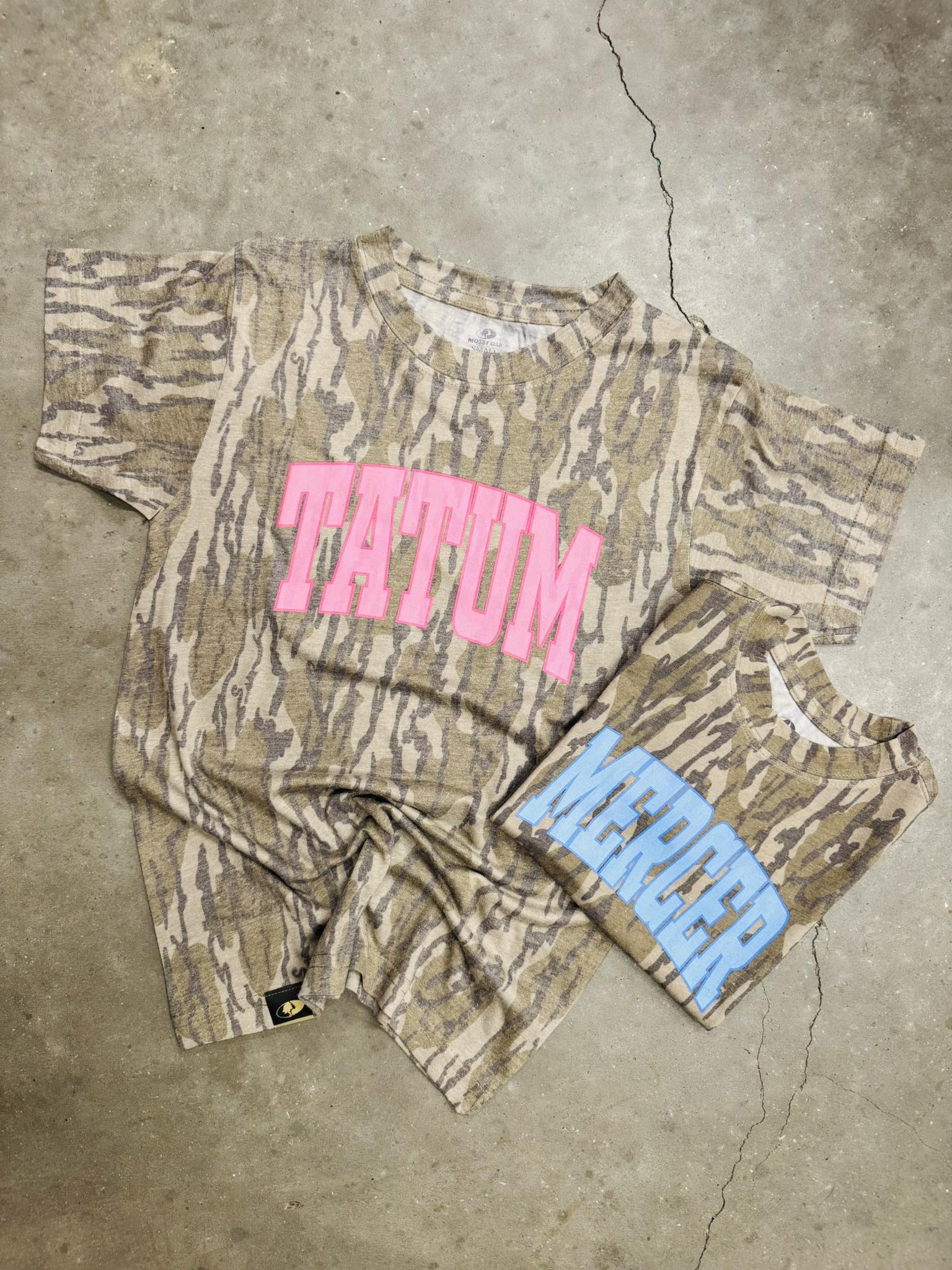 Camouflage t-shirt with pink text and blue shorts on a concrete floor