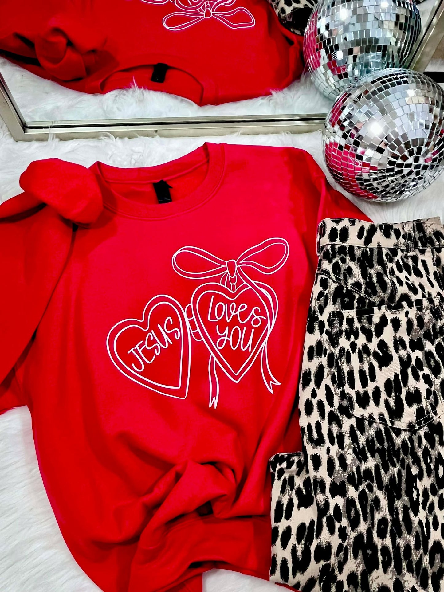 Red sweatshirt with 'I love you' design, leopard print pants, and disco balls on a white surface.