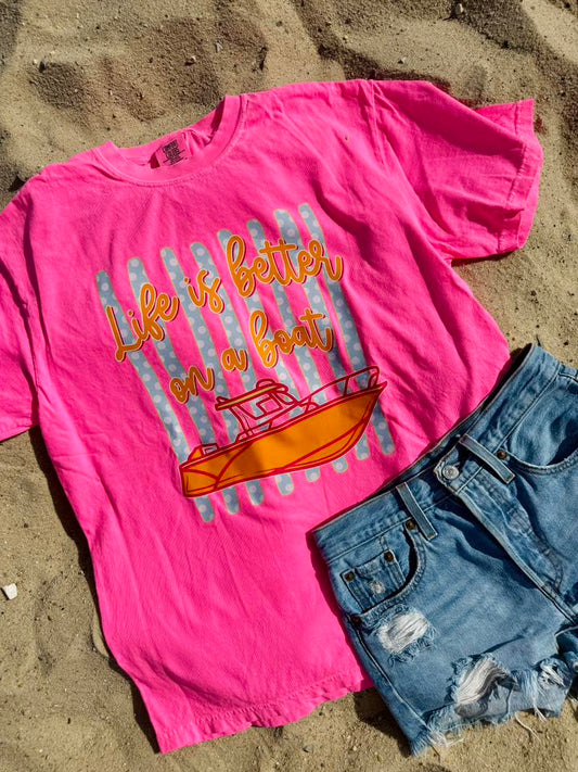 Pink t-shirt with 'Life is better on a boat' graphic and denim shorts on sand