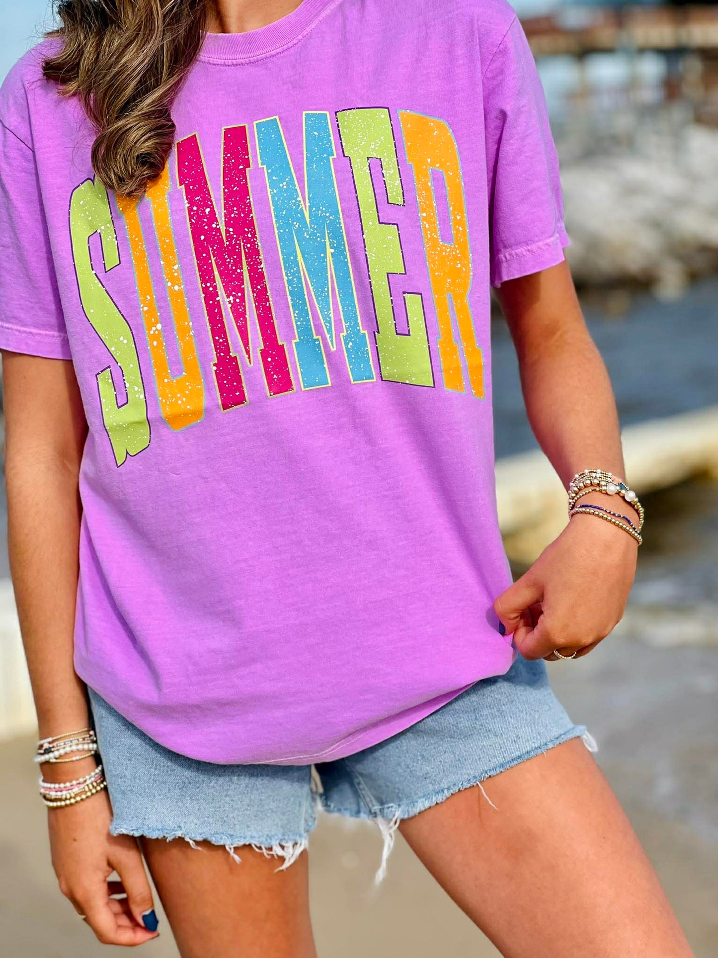 Person wearing a purple t-shirt with 'SUMMER' in colorful letters, standing outdoors.