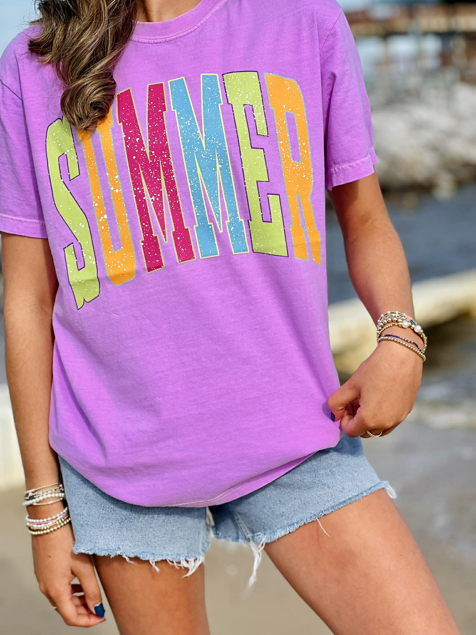 Person wearing a purple t-shirt with 'SUMMER' in colorful letters, standing outdoors.