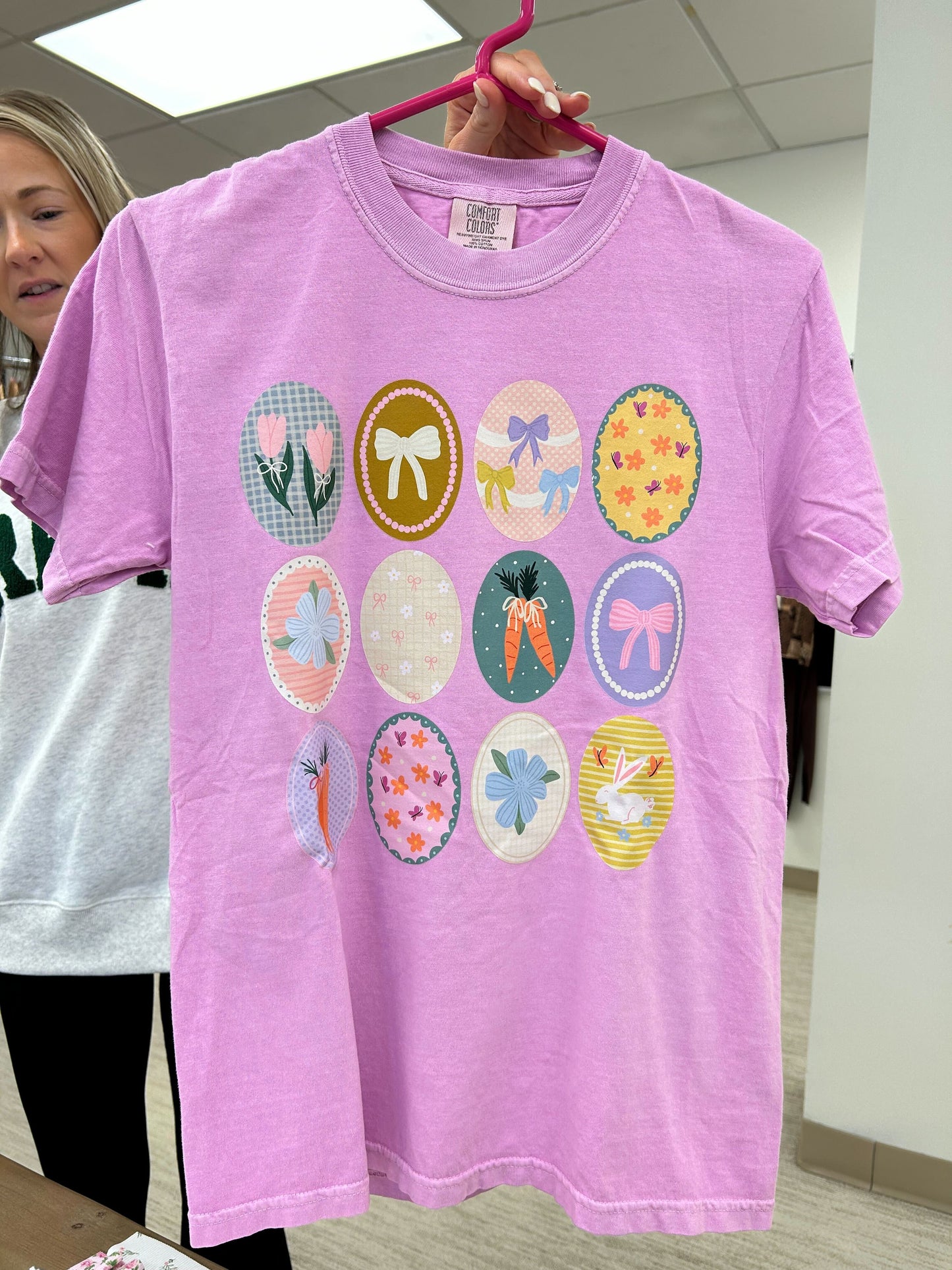 Purple t-shirt with colorful graphic designs on a hanger, held by a person.